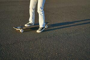 ritagliata tiro di gambe su longboard. pattinatore ragazza equitazione sua skateboard su strada. femmina adolescente su incrociatore foto