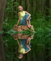 adolescenziale ragazza si siede su un' ceppo nel un' naturale foresta parco con un' triste e riflessivo Guarda, riflessa nel il acqua foto