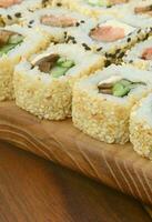 avvicinamento di un' lotto di Sushi rotoli con diverso otturazioni menzogna su un' di legno superficie. macro tiro di cucinato classico giapponese cibo con un' copia spazio foto