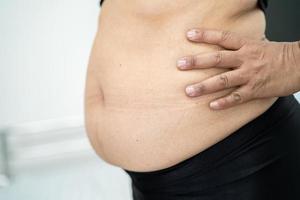 la donna asiatica in sovrappeso mostra la pancia grassa in ufficio. foto