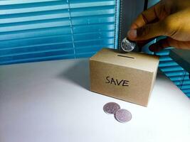 Salvataggio i soldi con mano mettendo monete nel un' scatola risparmi foto