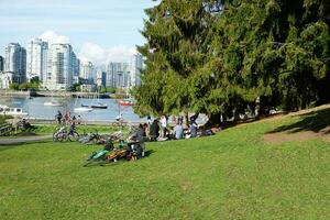 persone godendo un' soleggiato primavera giorno vicino il acqua nel il parco, con un' sbalorditivo paesaggio urbano nel il sfondo. Vancouver, avanti Cristo, Canada. Maggio 02, 2021. foto