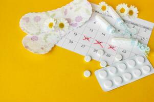 mestruale pastiglie e tamponi su mestruazione periodo calendario con camomille su giallo sfondo. foto