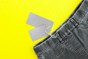 piatto posizione, dettaglio di nero jeans, vuoto grigio etichette su giallo sfondo. foto