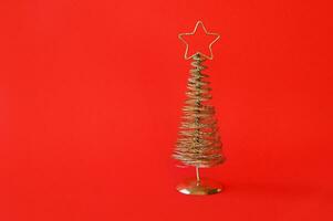 d'oro metallo Natale albero con un' stella su superiore, rosso sfondo. foto