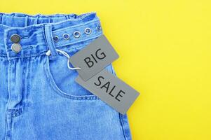 piatto posizione, dettaglio di denim jeans con grigio etichetta e iscrizione grande vendita su giallo sfondo. foto
