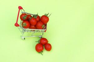 biologico ciliegia pomodori nel un' mini shopping carrello su un' leggero verde sfondo. foto