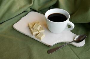 bianca tazza con fresco caffè con un' bianca bar di cioccolato con totale Nocciole. foto