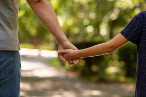 il Il padre di mano tenuto strettamente il mano di il suo poco figlio contro il sfondo di verde fogliame, avvicinamento foto