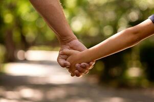 il Il padre di mano tenuto strettamente il mano di il suo poco figlio contro il sfondo di verde fogliame, avvicinamento foto