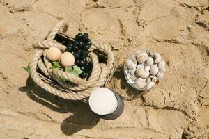 frutta siamo nel un' cestino, un' candela, mare pietre nel un' bicchiere vaso. arredamento di un' romantico cena di il mare o oceano foto