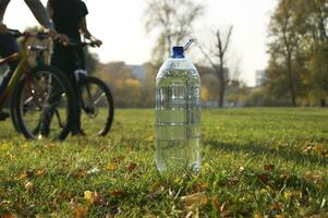 fresco acqua bottiglia nel il parco contro il sfondo di Due ciclisti. foto