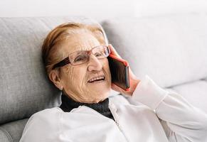 donna anziana sorridente che parla sullo smartphone a casa foto