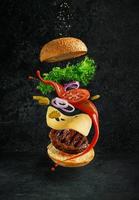 hamburger con ingredienti galleggianti su sfondo scuro. concetto di natura morta creativa e pubblicità foto