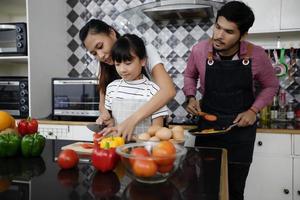 la famiglia felice ha papà, mamma e la loro piccola figlia che cucinano insieme in cucina foto