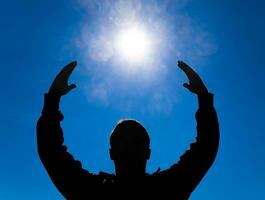 silhouette di un' uomo contro il sfondo di il sole e blu cielo. mani siamo sollevato su per il sole foto