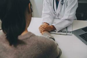 medico e paziente seduta vicino ogni altro a il tavolo nel clinica ufficio. il messa a fuoco è su femmina del medico mani rassicurante donna, solo mani, vicino su. medicina concetto foto