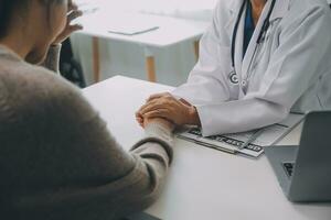 medico e paziente seduta vicino ogni altro a il tavolo nel clinica ufficio. il messa a fuoco è su femmina del medico mani rassicurante donna, solo mani, vicino su. medicina concetto foto