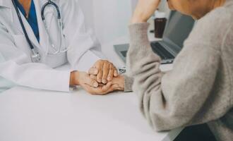 medico e paziente seduta vicino ogni altro a il tavolo nel clinica ufficio. il messa a fuoco è su femmina del medico mani rassicurante donna, solo mani, vicino su. medicina concetto foto