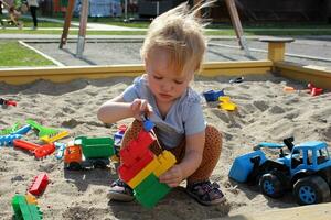 poco ragazza giochi nel il sandbox con giocattoli. foto