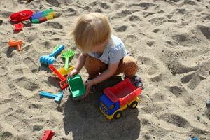 poco ragazza giochi nel il sandbox con giocattoli. foto