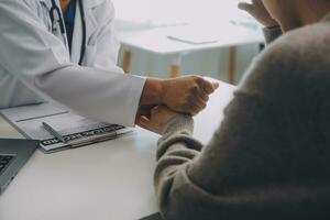 medico e paziente seduta vicino ogni altro a il tavolo nel clinica ufficio. il messa a fuoco è su femmina del medico mani rassicurante donna, solo mani, vicino su. medicina concetto foto