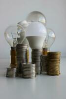 colonne di monete nel davanti di diverso lampadina lampade come un illustrazione elettricità costo foto