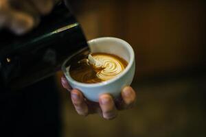 il primo piano delle mani il barista fa la pittura di arte del caffè del latte foto