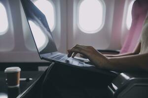 asiatico donna passeggeri seduta nel aereo vicino finestra e lettura notizia a partire dal sociale reti o utilizzando viaggio applicazioni nel smartphone foto