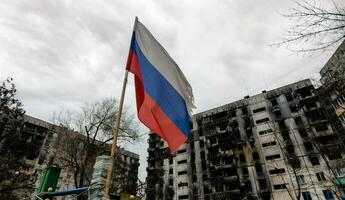 tricolore bandiera di Russia contro il sfondo di distrutto e bruciato case nel Ucraina foto