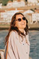 giovane donna che usa occhiali da sole sorridendo molto mentre li tocca, concetto di occhiali da sole, estate e viaggio, spazio copia