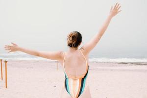 giovane donna in costume da bagno indietro, saltando e festeggiando durante una giornata di sole in spiaggia, libertà e concetto di vacanza, copia spazio foto