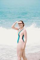 giovane donna in costume da bagno di fronte all'oceano che si gira verso la macchina fotografica e sorride, copia spazio, libertà e concetto futuro