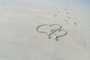 Due cuori su il spiaggia, tropicale luna di miele o anniversario. disegno nel sabbia con passi. romantico viaggio concetto foto