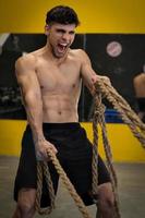 muscoloso potente uomo aggressivo che si allena con la corda in palestra per il fitness di allenamento funzionale foto