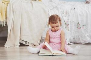 la bellissima bambina legge un libro con il suo orsetto preferito su una morbida coperta di peluche foto