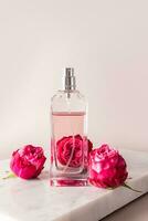 un elegante bottiglia di Da donna profumo o eau de Toilette sta su un' bianca marmo podio tra leggere boccioli di rosa. verticale Visualizza. un' copia spazio. pastello foto