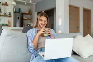 positivo giovane donna libero professionista Guardando video nel blog su netbook e avendo un' caffè a confortevole casa. bellissimo giovane attività commerciale donna Lavorando su libero professionista collegamento per Internet foto