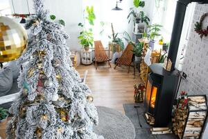 festivo bianca moderno interno di Casa è decorato per Natale e nuovo anno nel soffitta stile con nero fornello, il camino, Natale albero. in vaso impianti, legna da ardere nel il catasta di legna foto