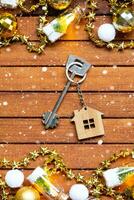 chiave per Casa con un' portachiavi minuscolo casa su di legno sfondo con Natale arredamento disposizione. regalo per nuovo anno, Natale. costruzione, progetto, in movimento per nuovo Casa, mutuo, affitto e Acquista vero tenuta foto