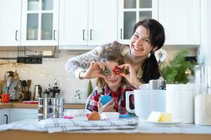 mamma e figlia nel il bianca cucina siamo preparazione biscotti per Natale e nuovo anno. famiglia giorno, preparazione per il vacanza, imparare per cucinare delizioso pasticcini, essi hold biscotto frese piace bicchieri foto