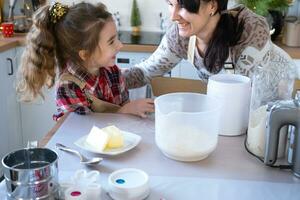 mamma e figlia nel il bianca cucina siamo preparazione biscotti, Inserisci ingredienti. famiglia giorno, preparazione per il vacanza Natale, imparare per cucinare delizioso pasticcini, tagliare forme su di Impasto con muffe foto