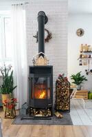 metall nero fornello, ardente focolare camino nel bianca festivo interno di Casa è decorato per Natale e nuovo anno, Natale albero. legna da ardere nel il catasta di legna, accogliente e riscaldamento di casa foto