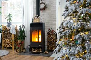 metall nero fornello, ardente focolare camino nel bianca festivo interno di Casa è decorato per Natale e nuovo anno, Natale albero. legna da ardere nel il catasta di legna, accogliente e riscaldamento di casa foto