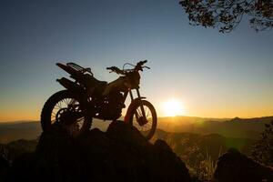 uomo con motocross bicicletta contro bellissimo luci, silhouette di un' uomo con motocross motociclo su superiore di roccia alto montagna a bellissimo tramonto, enduro motociclo viaggio concetto. foto
