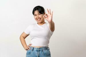 il allegro giovane asiatico donna sorridente e mostrando il ok mano cartello in piedi su bianca sfondo. foto
