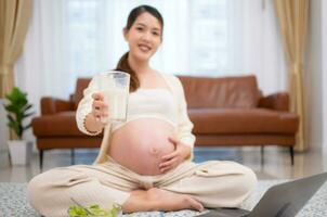 incinta donna potabile latte mentre seduta su il pavimento a casa foto