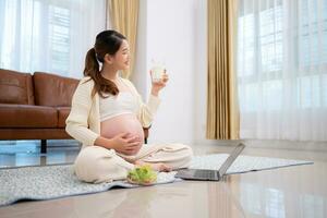 incinta donna potabile latte mentre seduta su il pavimento a casa foto