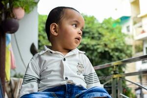 bambino ragazzo a casa balcone. luminosa ritratto di contento bambino seduta su il tavolo. poco 1 anno vecchio ragazzo durante il giorno leggero a Casa balcone. foto