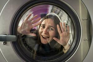 giovane donna nel il lavanderia camera avendo divertimento nel il lavaggio macchina tamburo foto